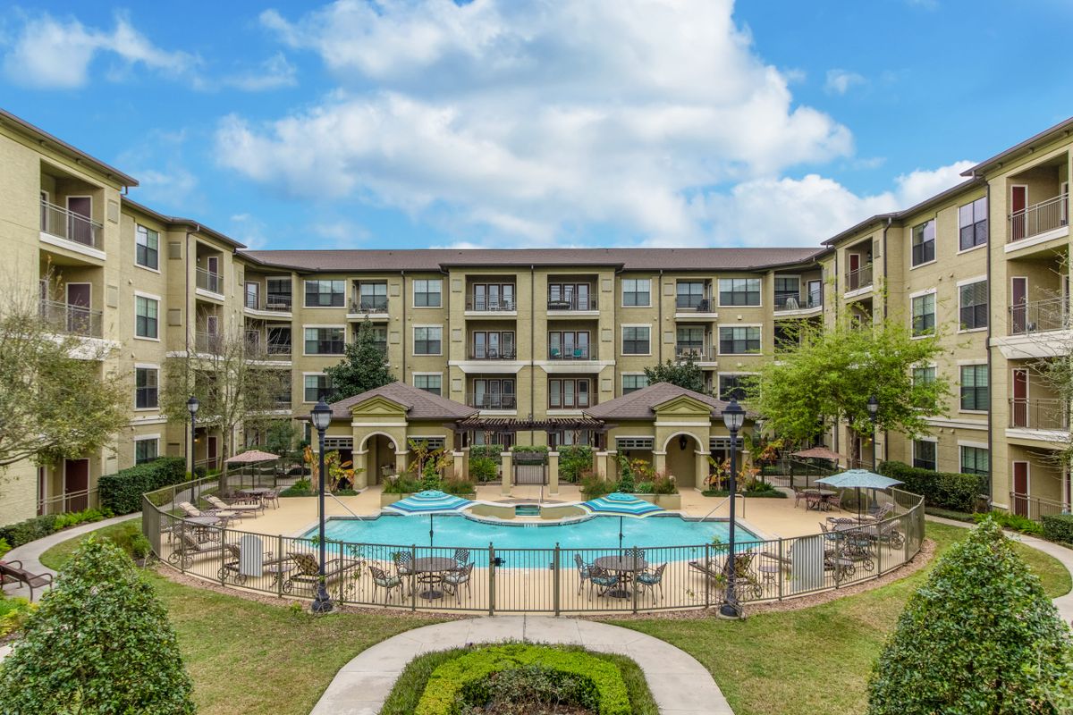 A luxurious apartment complex featuring a central swimming pool surrounded by lush landscaping.