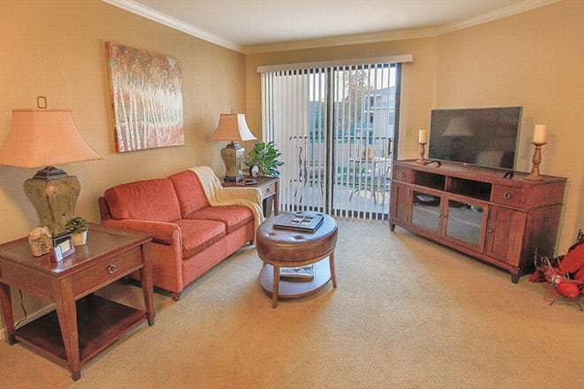 A cozy living room with a sofa, coffee table, and television, featuring a sliding glass door leading to a balcony.