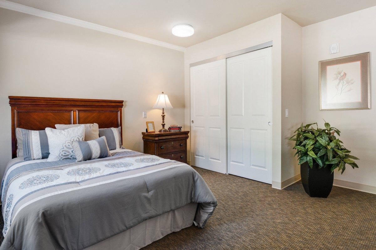 A cozy bedroom with a neatly made bed, nightstand, lamp, and closet.