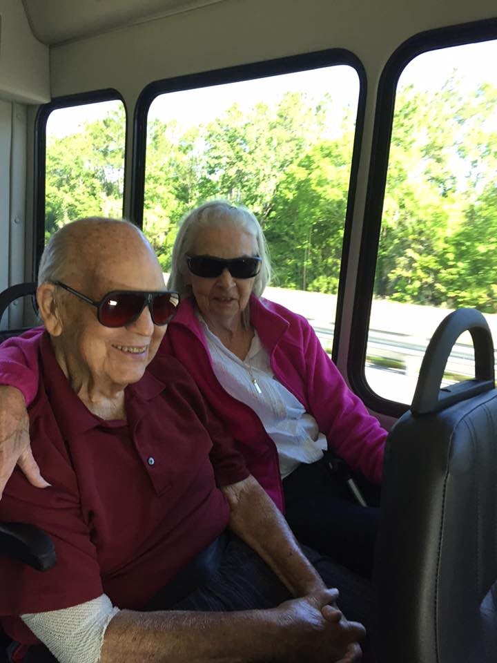 An elderly couple enjoying a bus ride together, both wearing sunglasses on a sunny day.