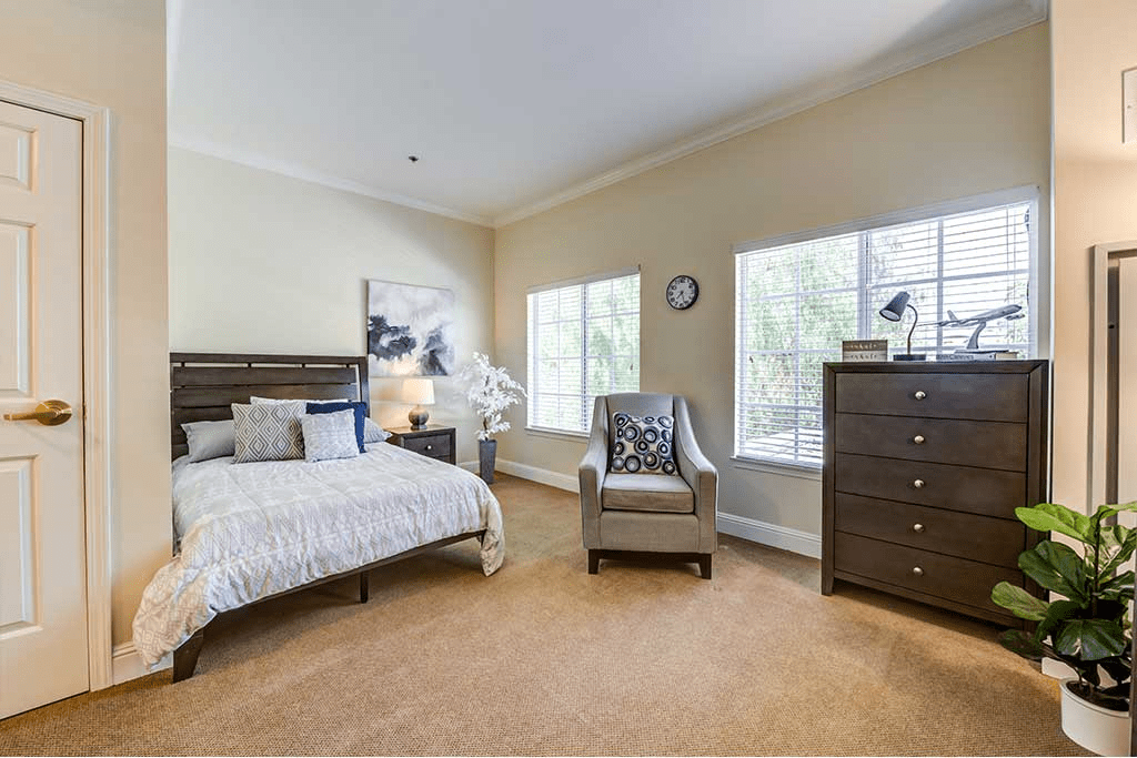 A well-lit bedroom with modern furnishings, including a bed, armchair, and dresser.