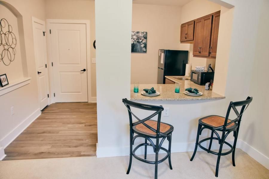 A cozy kitchen with bar stools and a counter setup, featuring wooden cabinets and modern decor.