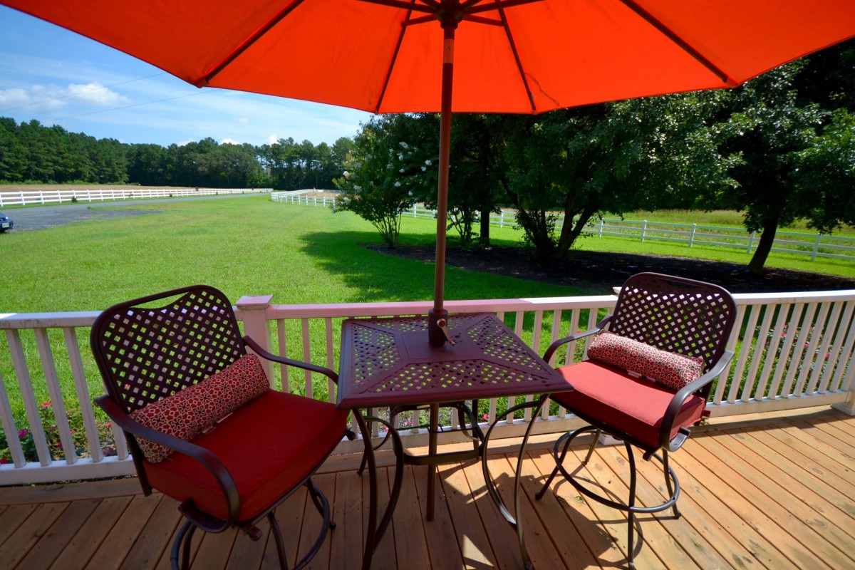 A sunny deck with patio furniture including an umbrella, chairs, and a table overlooking a green lawn.