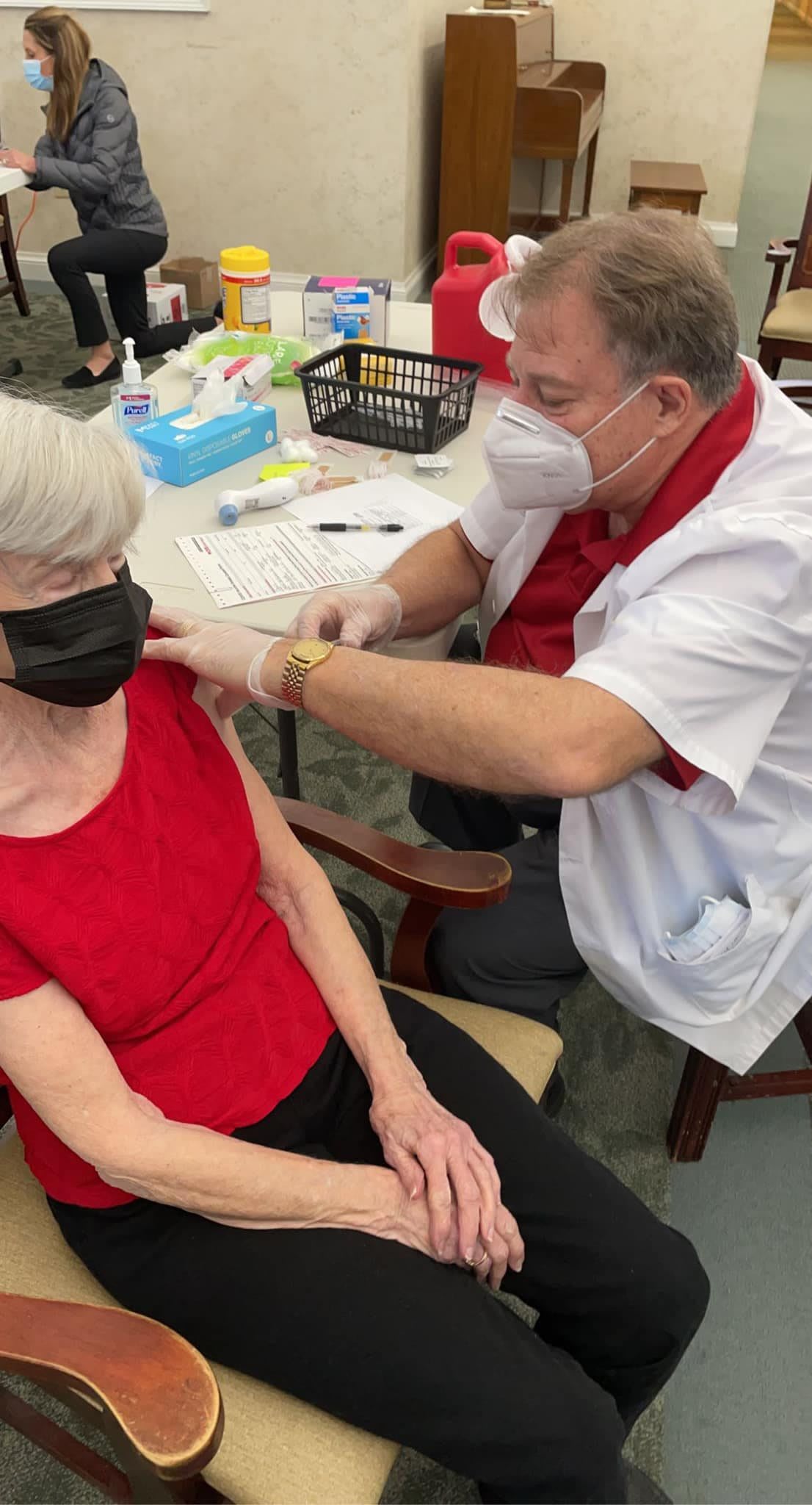 A healthcare professional administers a vaccine to an elderly person wearing a mask.
