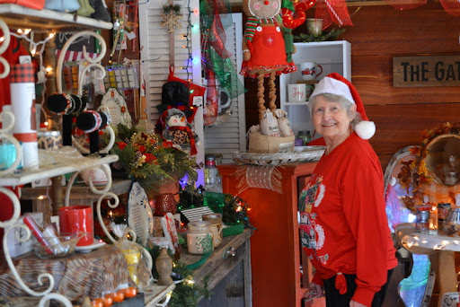 A cheerful individual in a Santa hat and festive red shirt stands amidst a vibrant display of Christmas decorations.