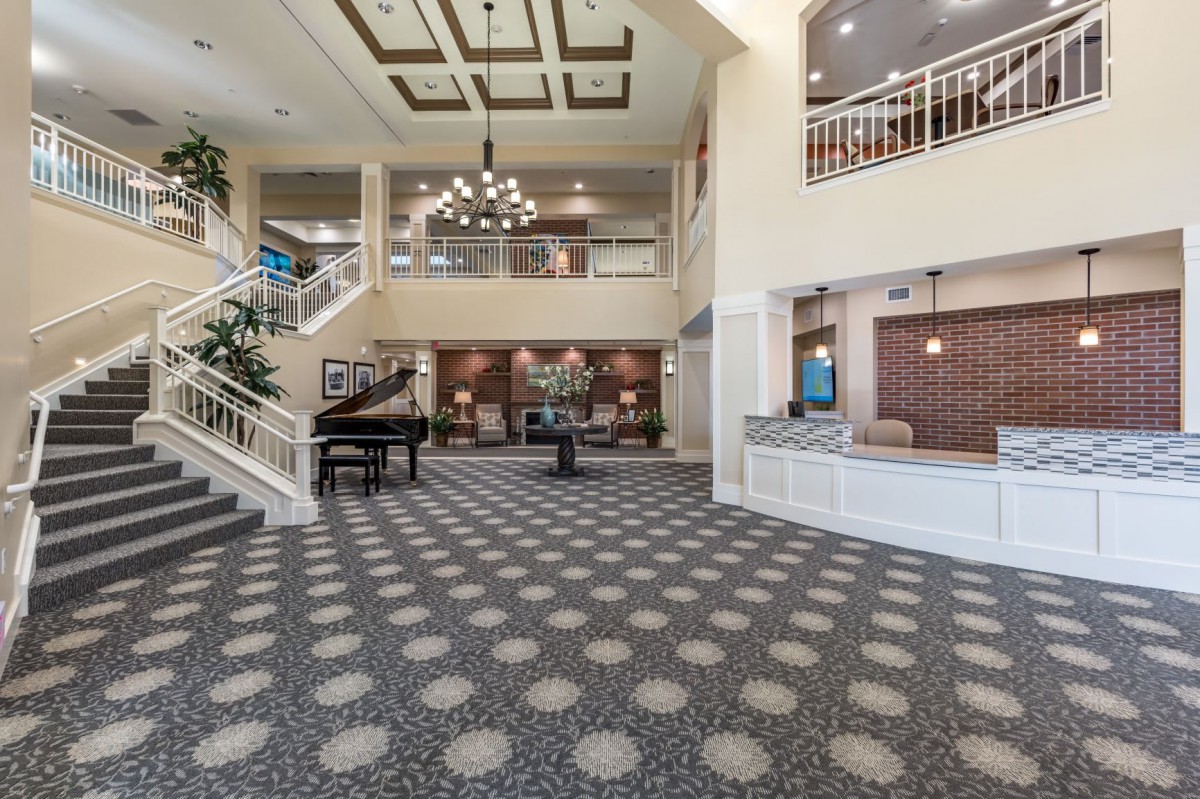 A spacious lobby with modern decor, featuring a grand piano, chandelier, and reception desk.