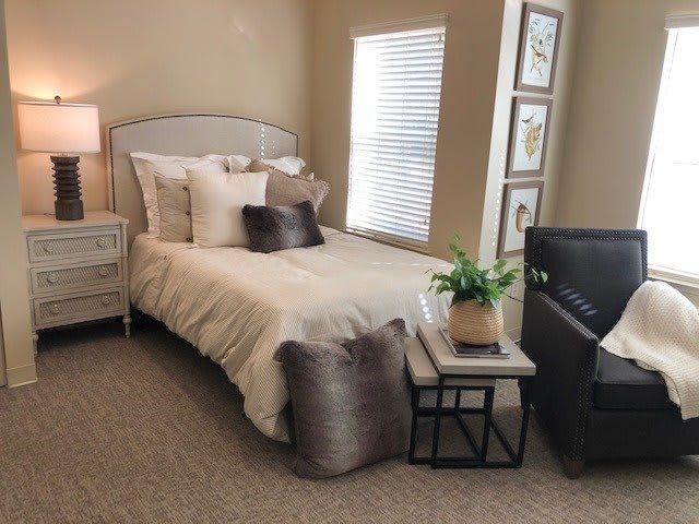 A cozy bedroom with neutral tones featuring a bed, nightstand, and decorative pillows.