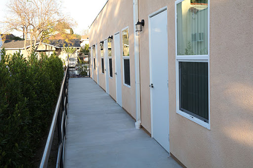 A view of a building's exterior featuring multiple doors and windows along a concrete walkway.