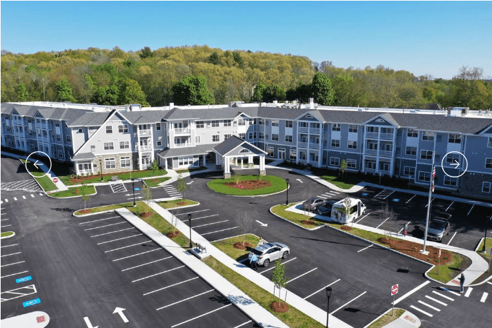 Aerial view of a large residential building with surrounding greenery and a parking lot.