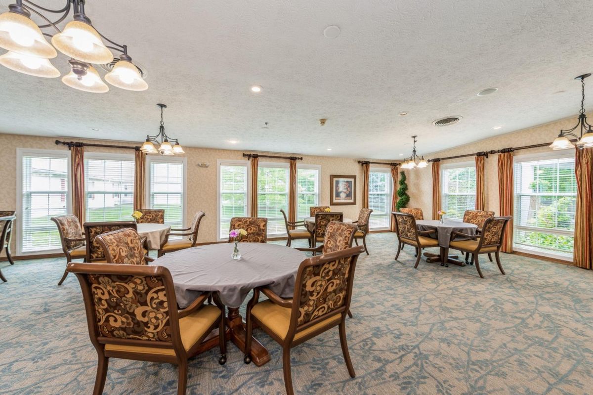 A spacious dining room with elegantly set tables and chairs, featuring large windows and decorative lighting.