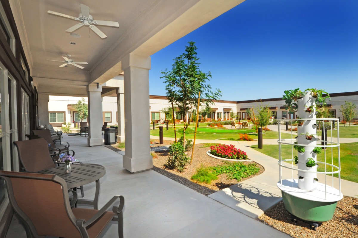A beautifully landscaped courtyard with a covered seating area and garden under a bright blue sky.
