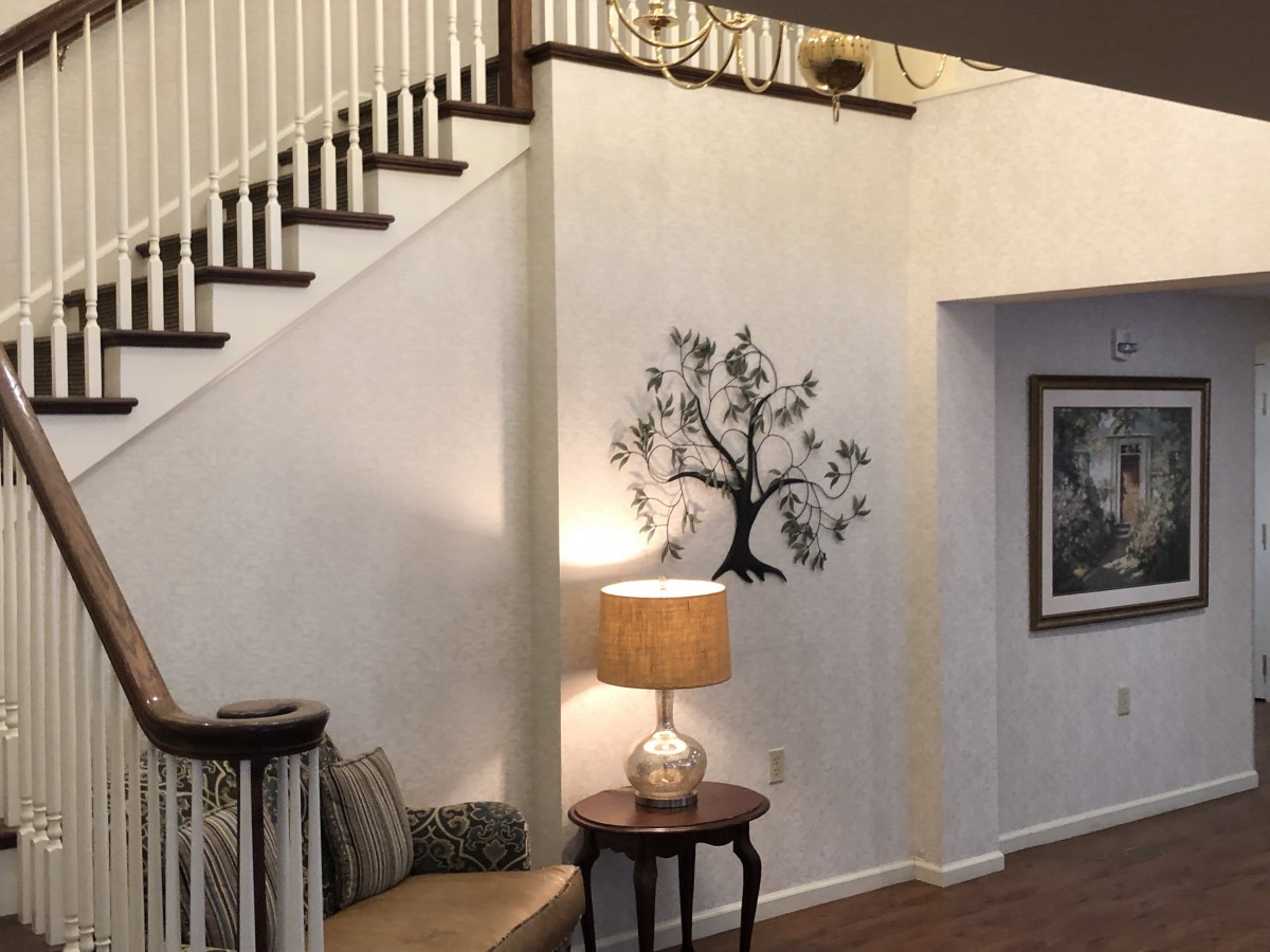 A cozy living room featuring a staircase, wall art, and comfortable seating with a lamp.