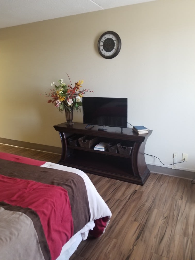 A cozy bedroom with a small television on a wooden stand, accompanied by a decorative flower vase.
