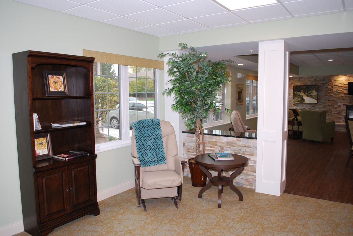 A cozy living room corner with a chair, small table, and bookshelf beside a window.