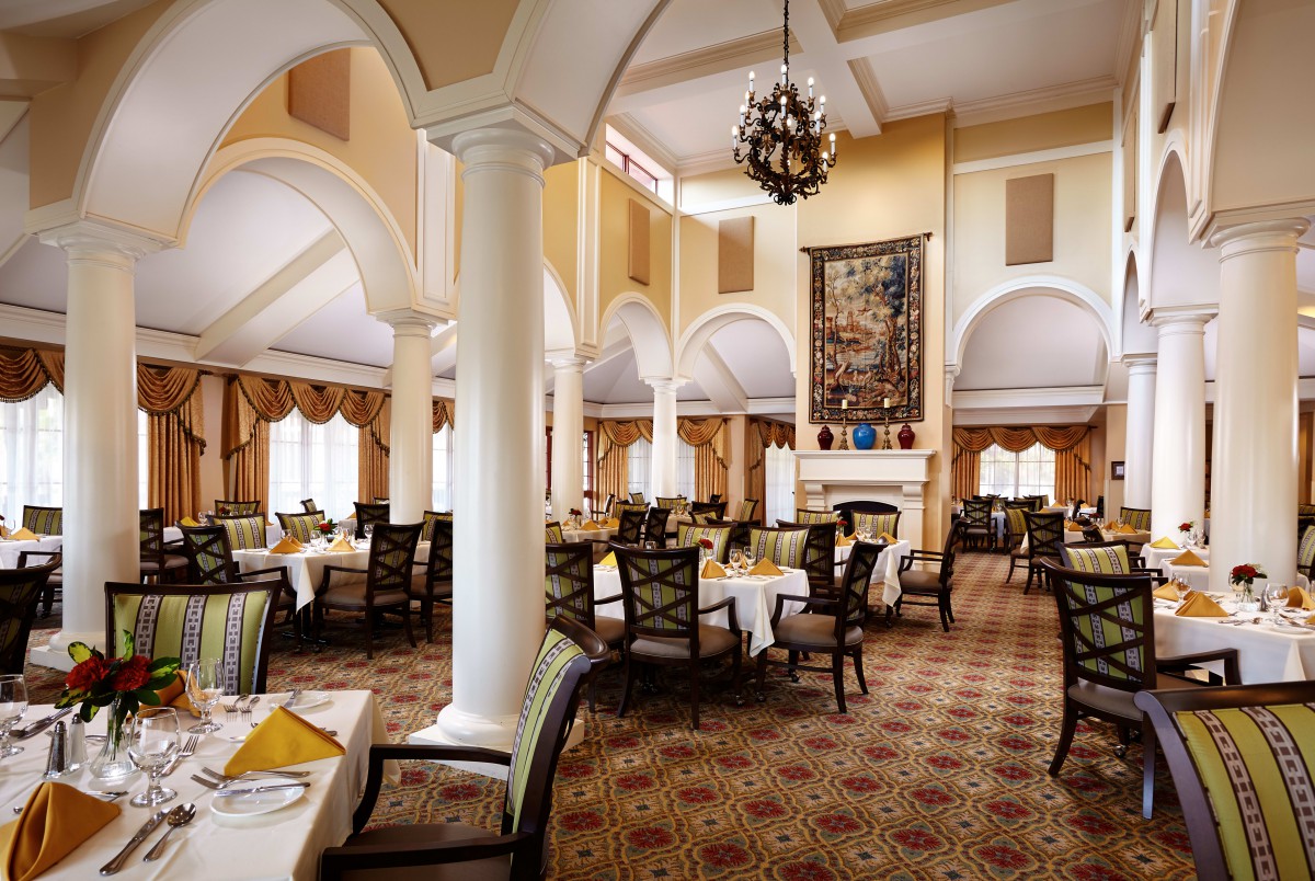 An elegant dining room with arches, set with tables and chairs, featuring a chandelier.