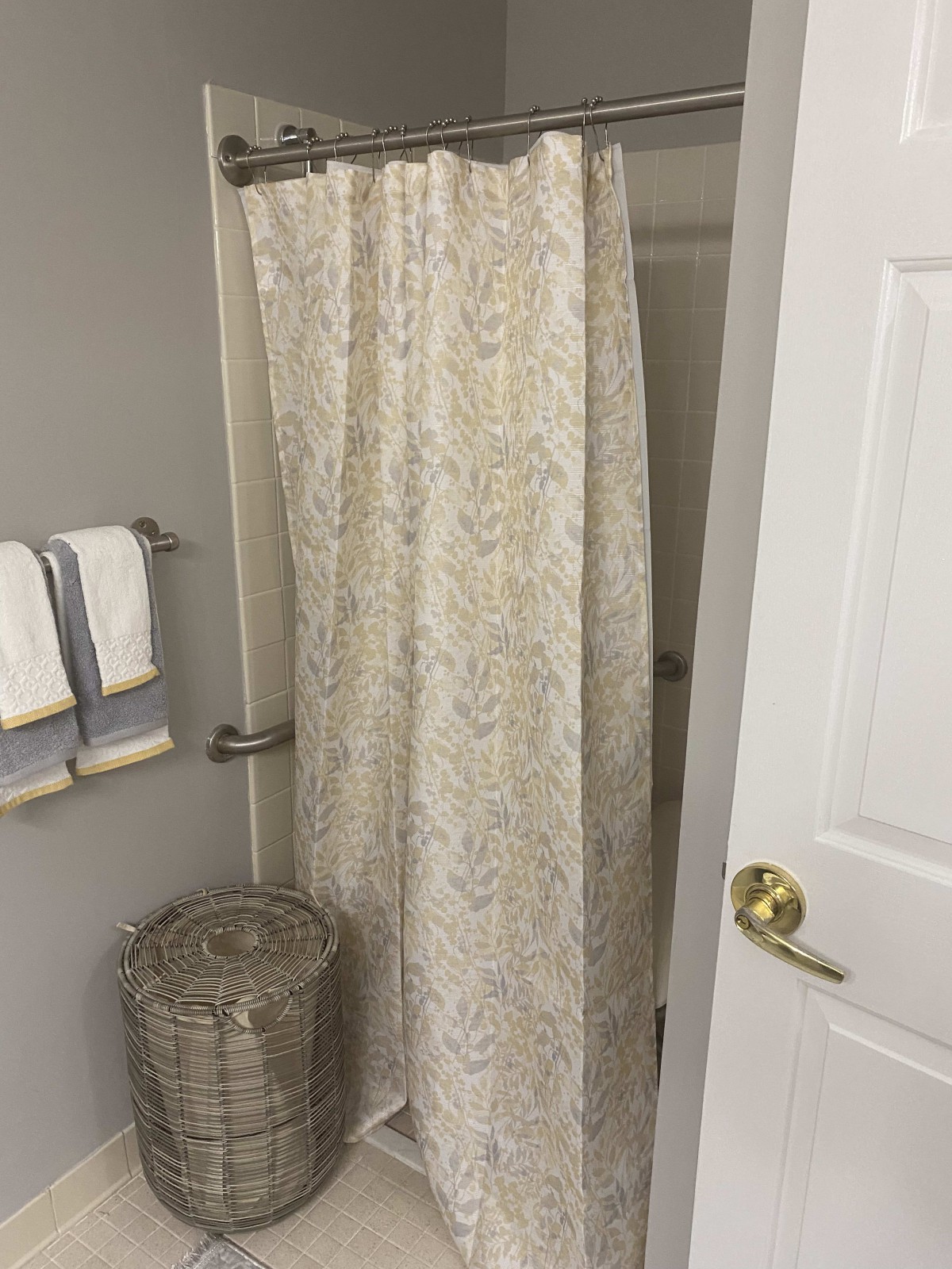 A bathroom with a patterned shower curtain, towels on a rack, and a wastebasket.