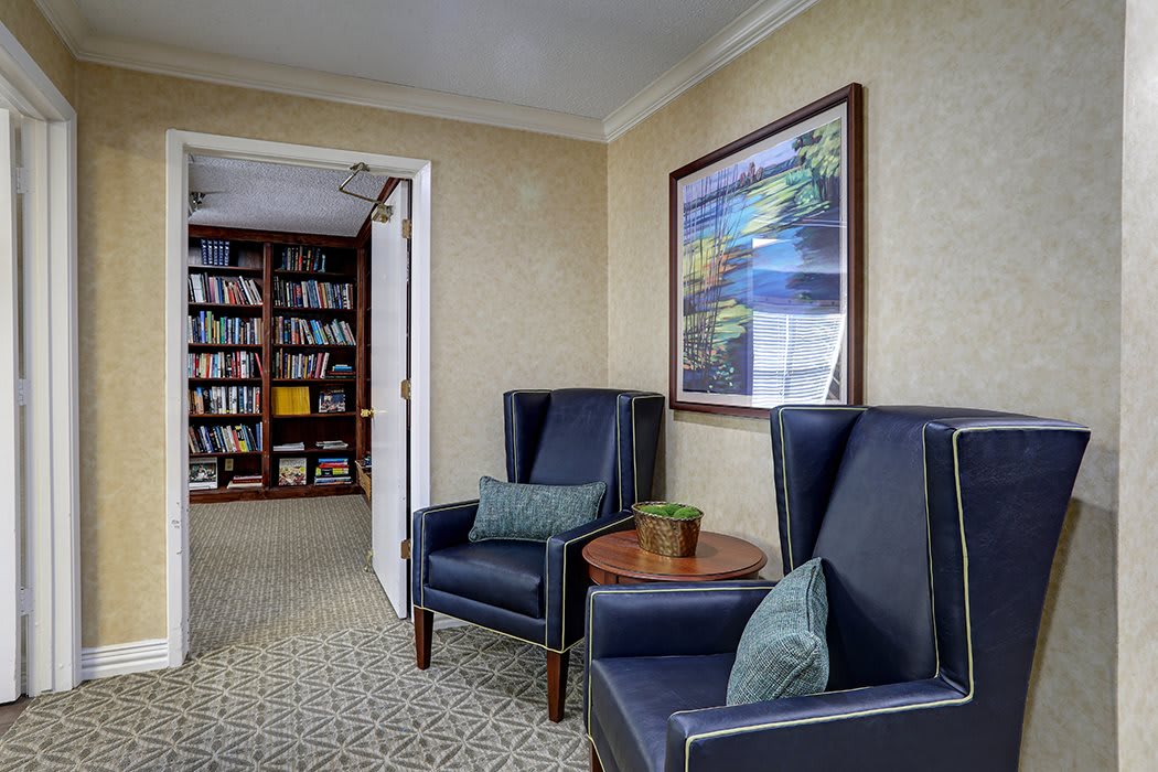 A cozy lounge area with two armchairs, a small side table, and a bookshelf filled with books.