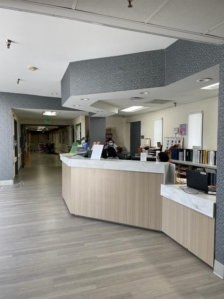 A hospital reception area with a front desk and office equipment, leading to a corridor.