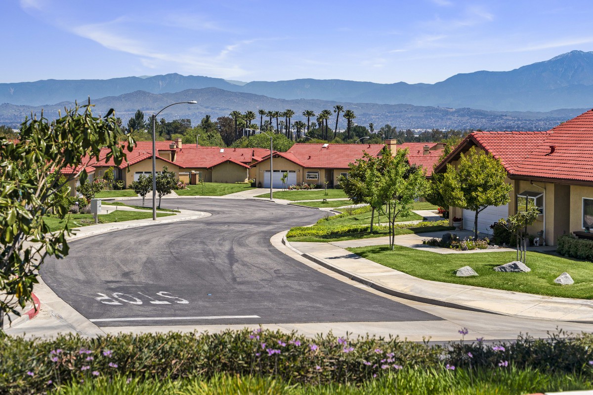 A peaceful suburban neighborhood with red-roofed houses and a mountain backdrop.