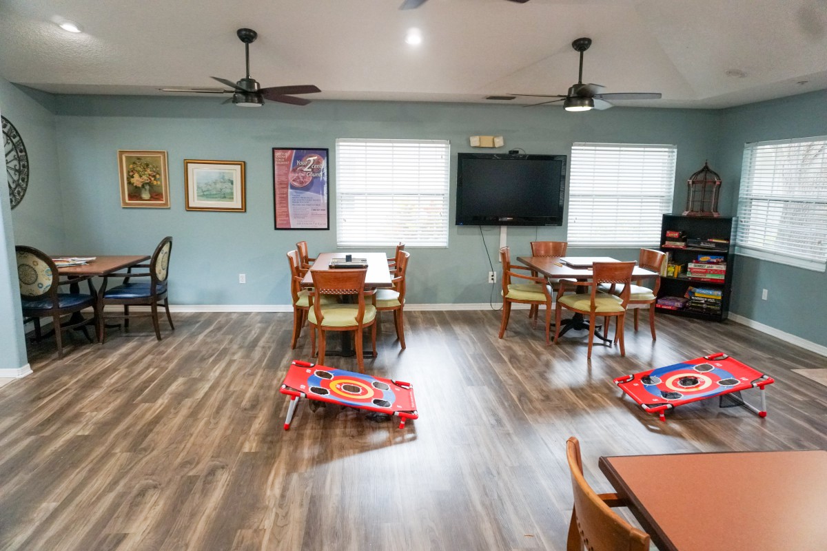 A spacious room with multiple tables and chairs, decorated with artwork on the walls and featuring wooden flooring.