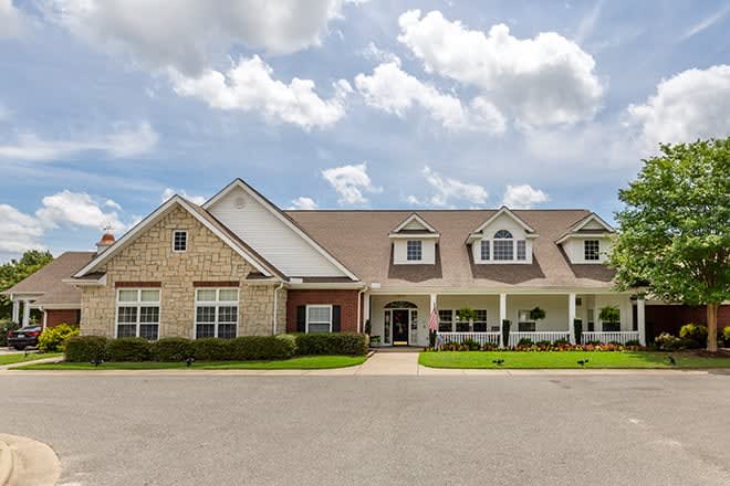 A large residential house with a well-maintained lawn under a partly cloudy sky.