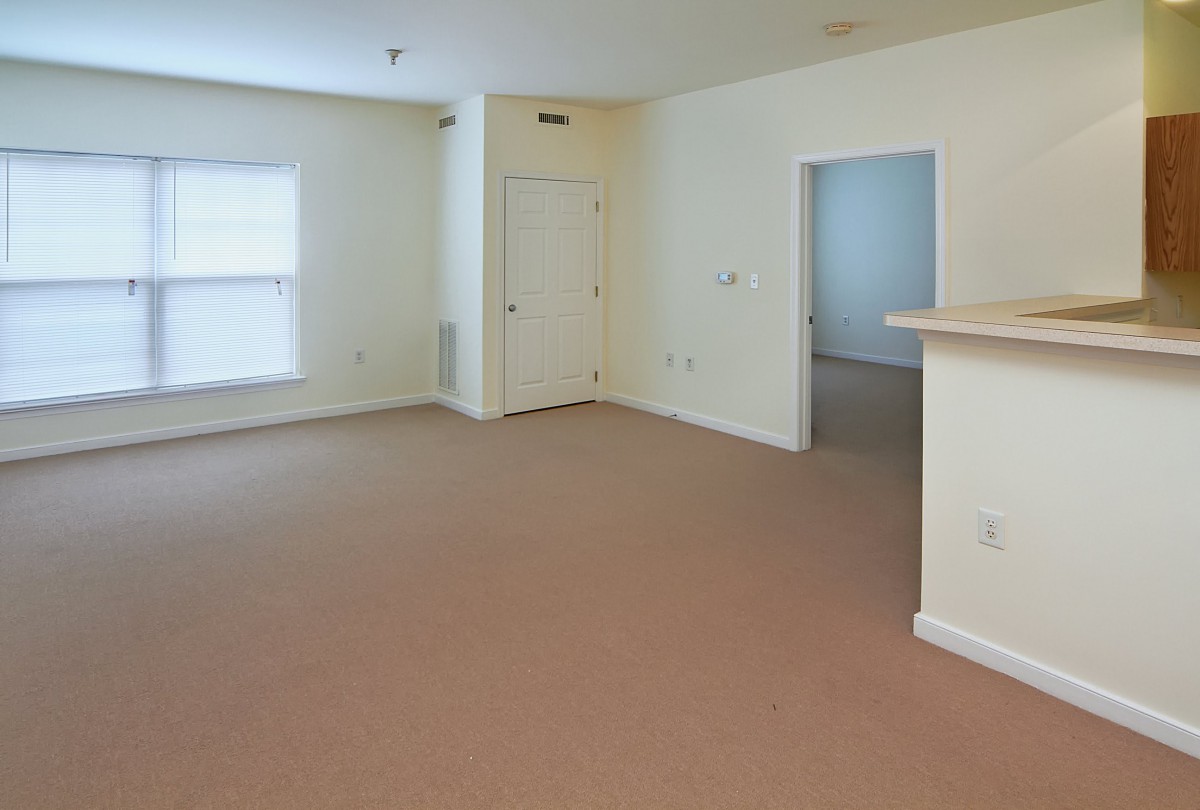 An empty, carpeted room with white walls and a window.