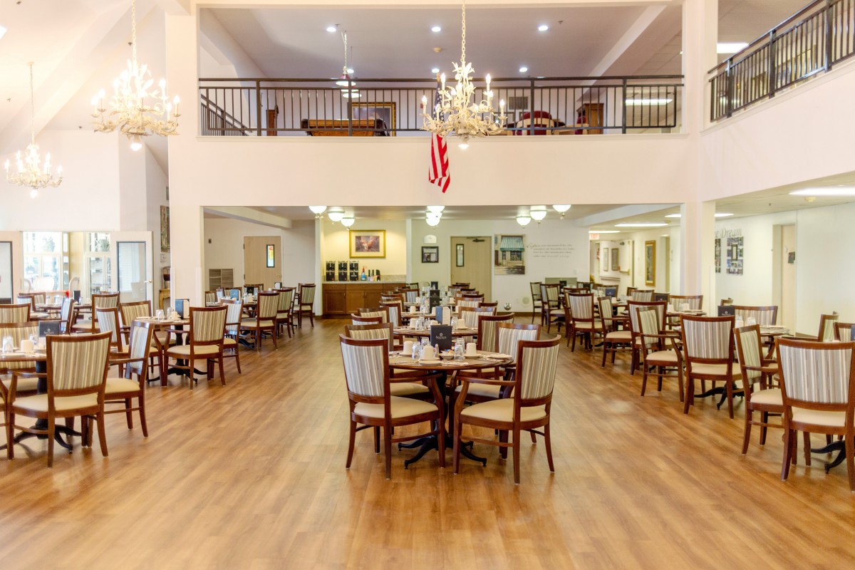 A spacious dining area with elegant chandeliers, wooden floors, and neatly arranged tables and chairs.