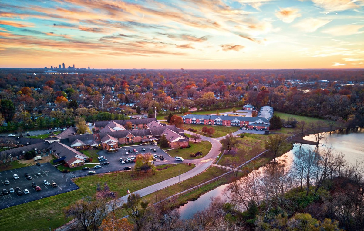 A beautiful aerial view of a suburban neighborhood at sunset in autumn, with houses, a river, and colorful trees under a cloudy sky.