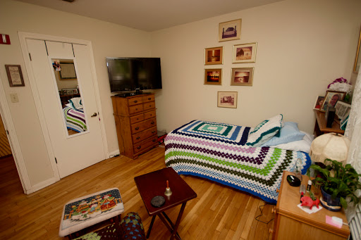 A cozy bedroom featuring a colorful crochet blanket on the bed, a TV mounted on the wall, and decorative photographs hanging above.