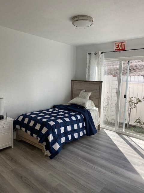 A minimalist bedroom with a single bed and a large sliding glass door allowing natural light to fill the room.