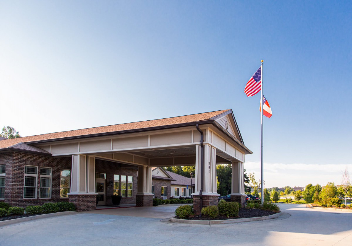 A building entrance with two flags, surrounded by neatly trimmed landscaping under a clear blue sky.