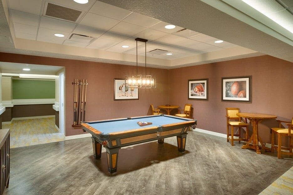 A stylish billiards room featuring a blue pool table, framed artwork, and a modern lighting fixture.