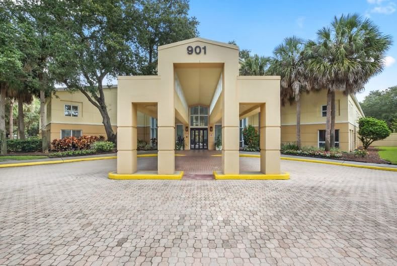 A building entrance with a covered driveway and surrounding palm trees.