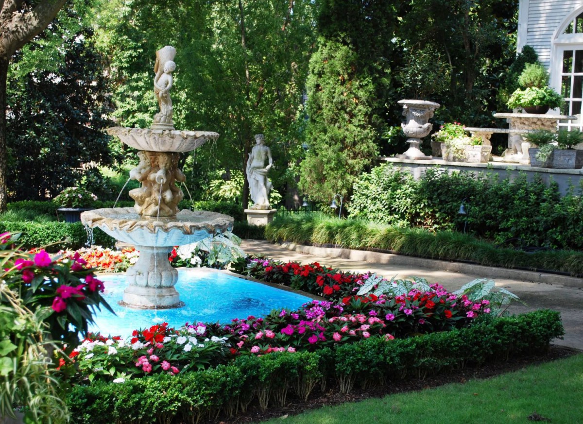 A serene garden scene featuring a central fountain surrounded by vibrant flowers and lush greenery, with a classical statue in the background.