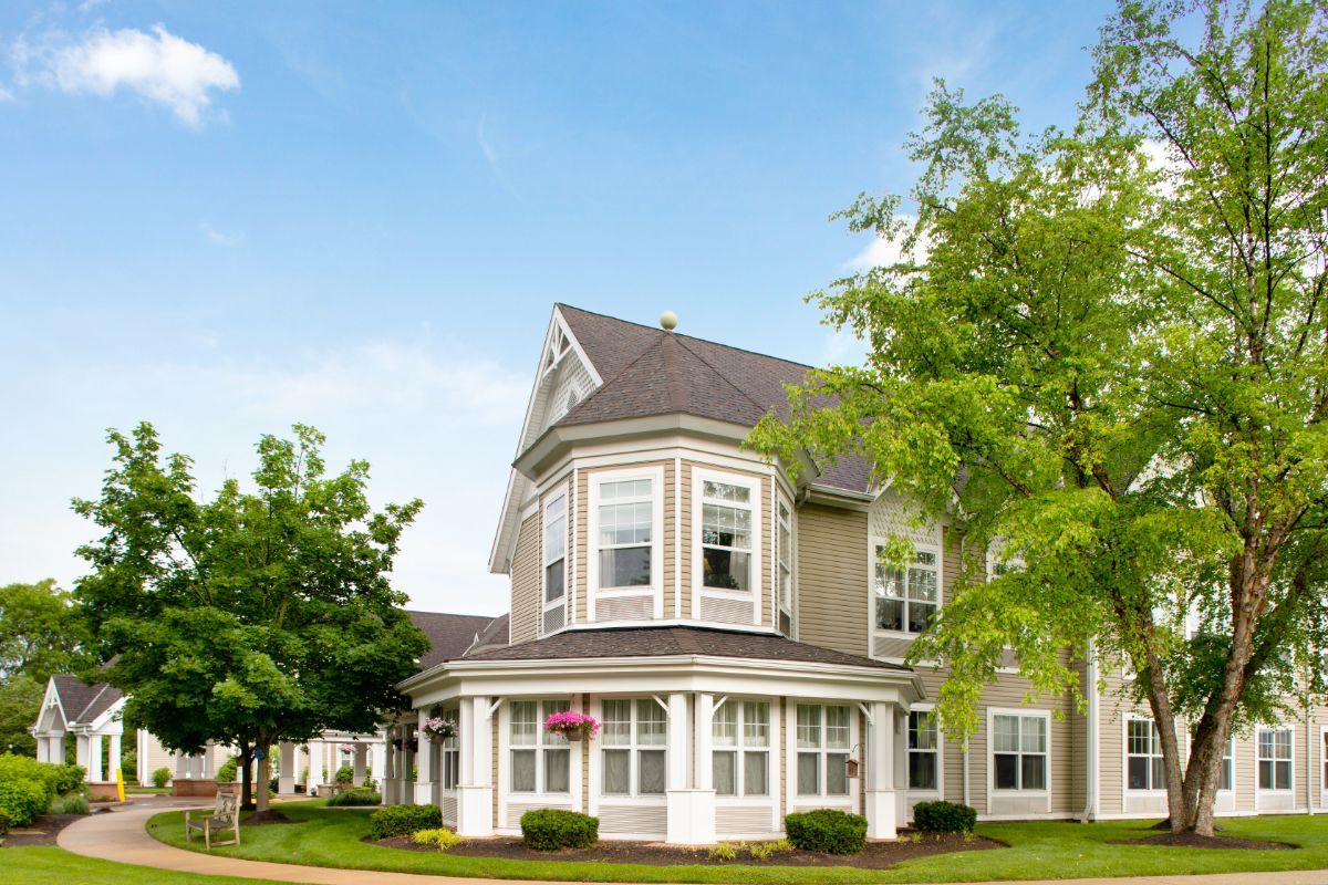 A beautiful Victorian-style house with a lush green lawn and trees under a clear blue sky.