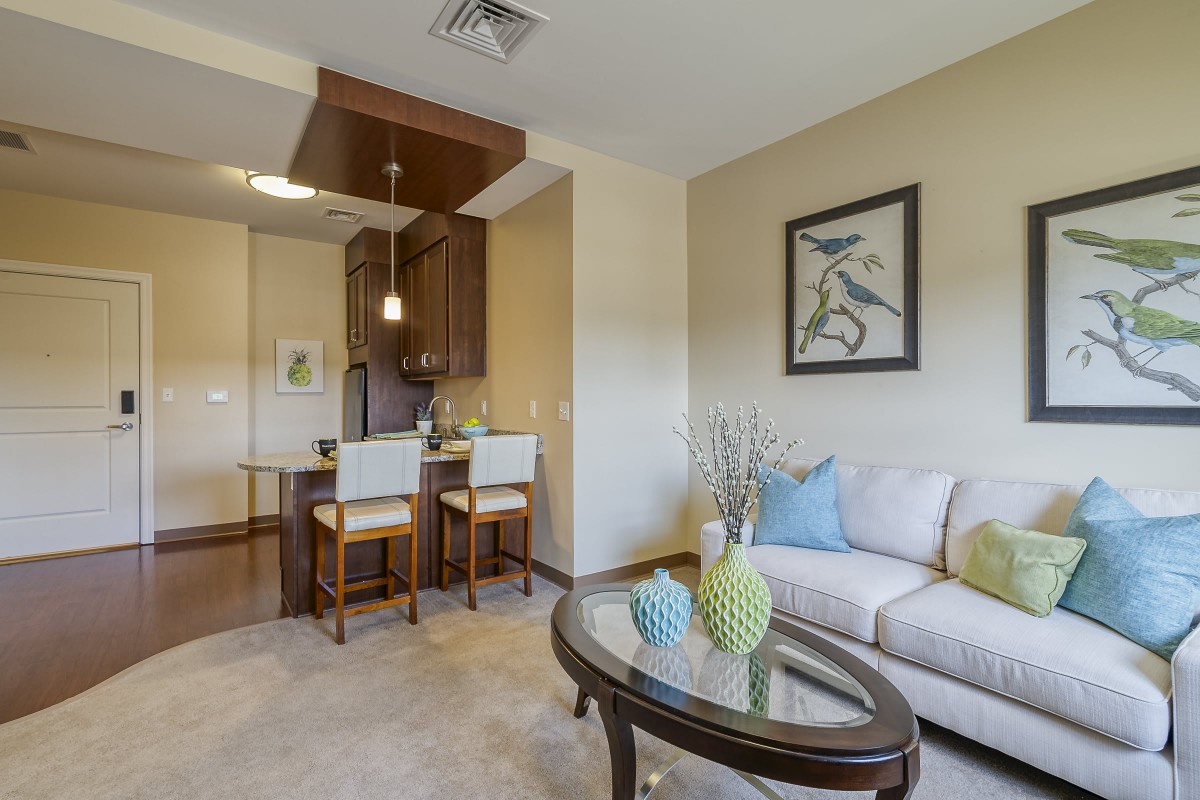 A modern living room with an open concept kitchen, featuring a comfortable sofa, decorative vases on a coffee table, and bar stools at the kitchen counter.