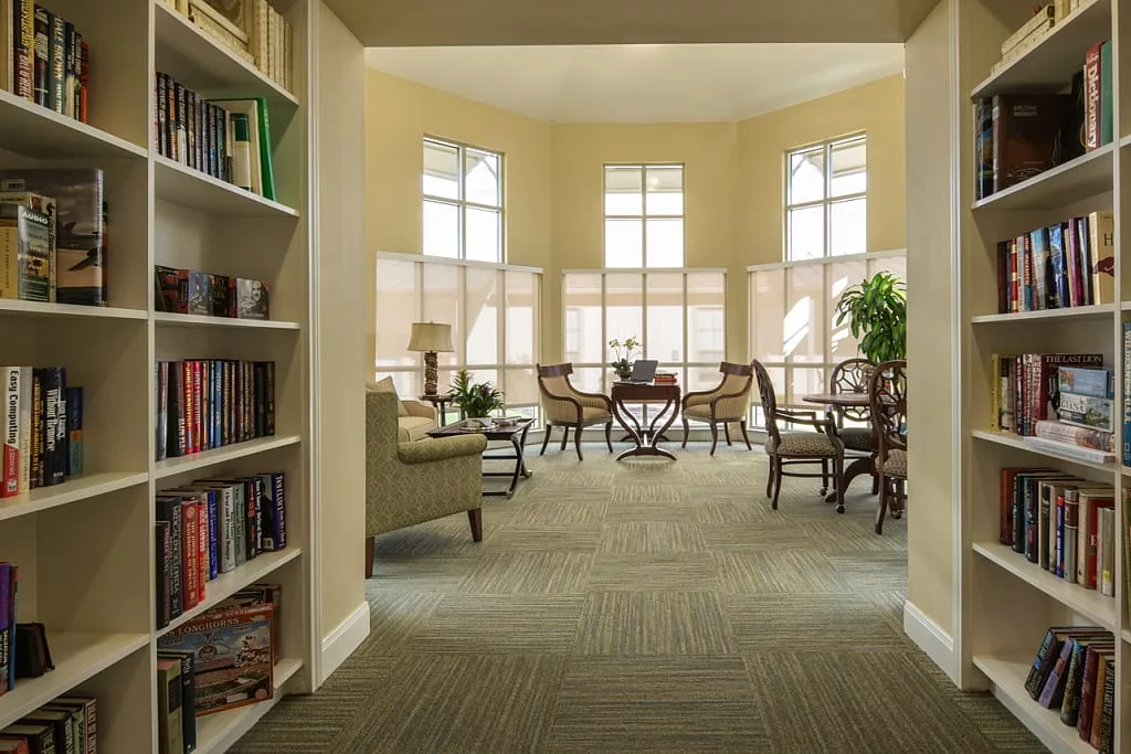 A cozy library reading area with large windows, bookshelves, and seating.