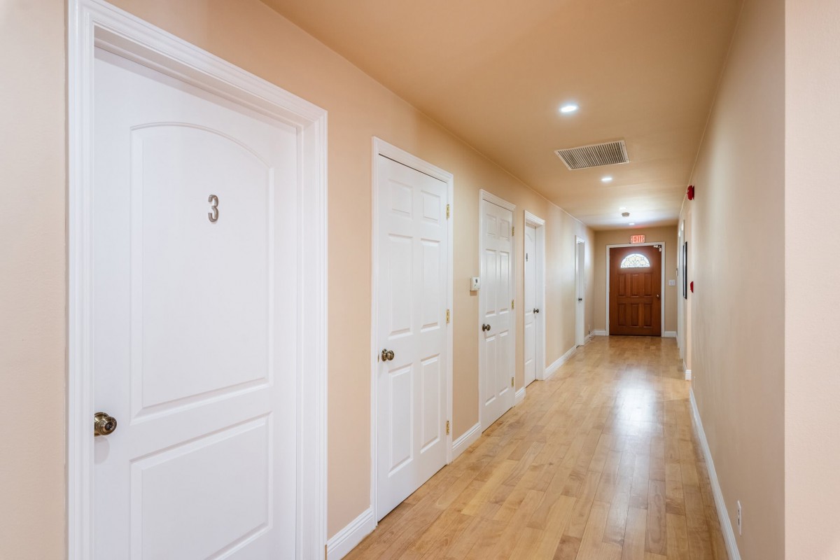 A long hallway with several white doors and wooden flooring.