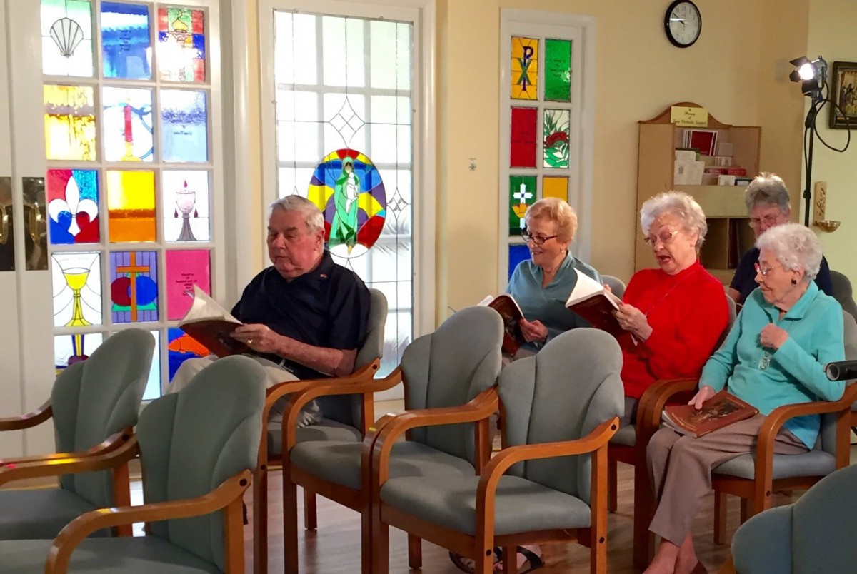A group of seniors sitting indoors, engaging in a reading activity together.