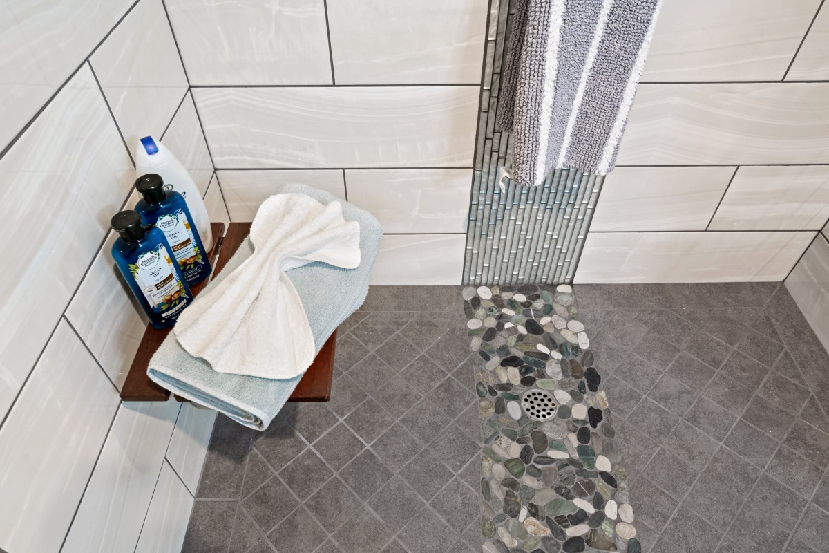 A modern bathroom with a tiled shower area, neatly folded towels, and shampoo bottles.