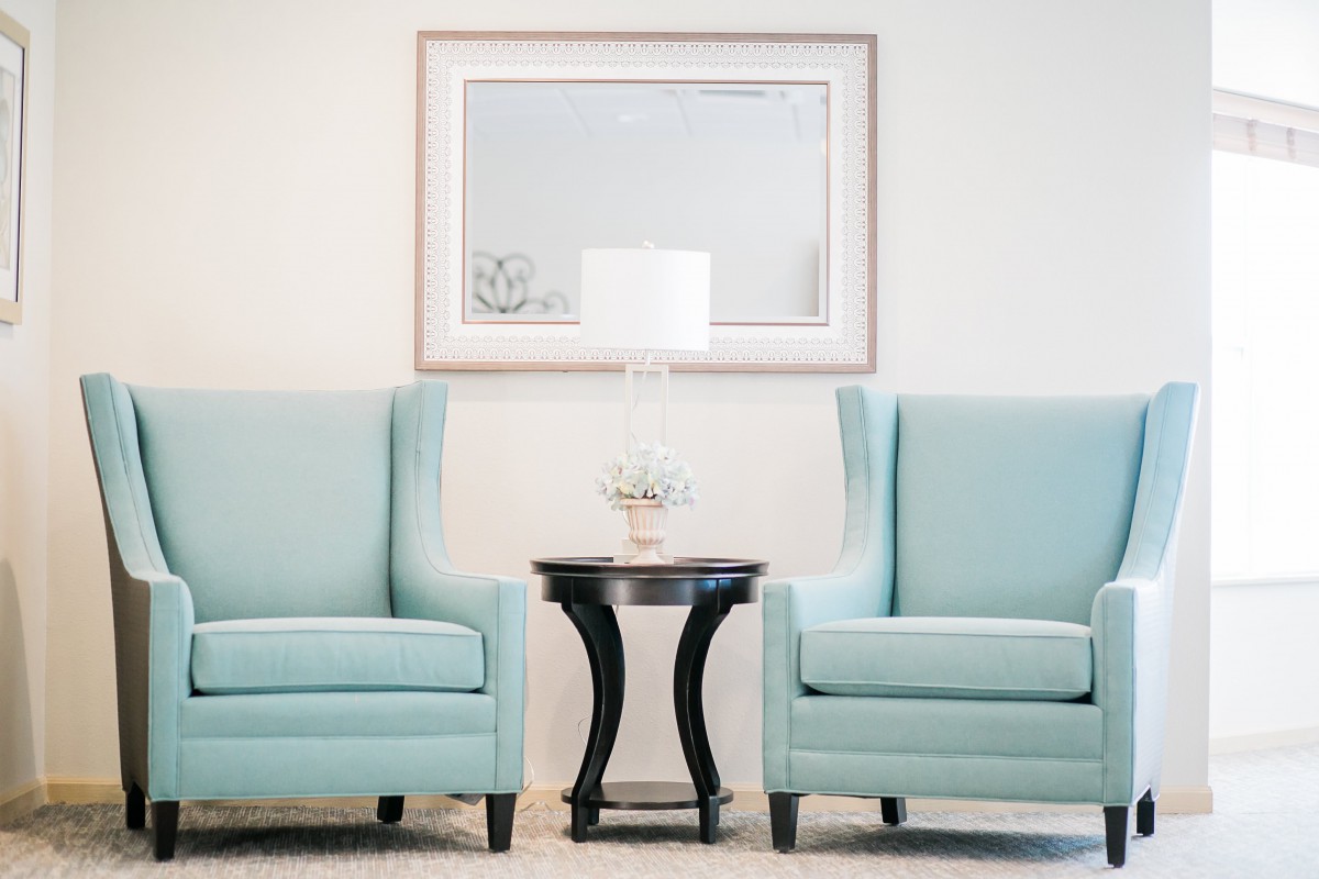 A minimalist living room setup with two blue chairs, a small round table, and a white lamp between them.