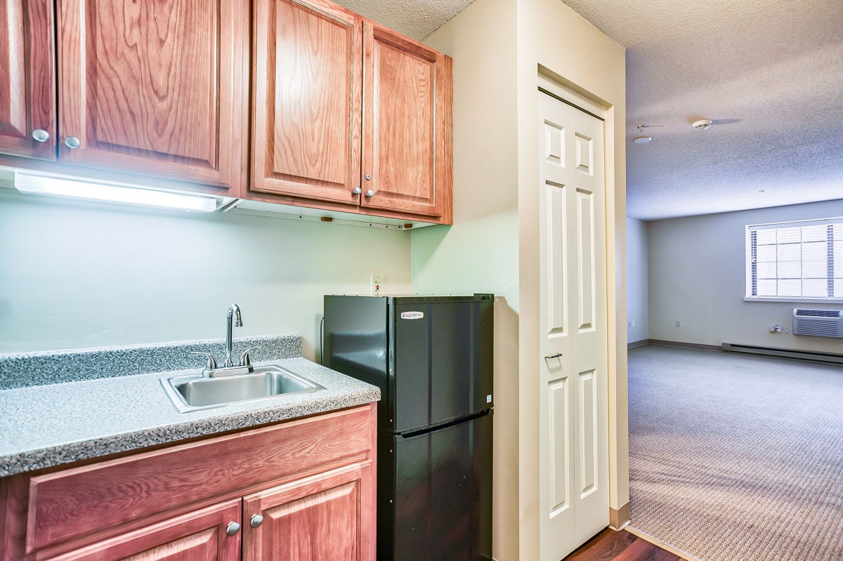 A compact kitchen area with wooden cabinets, a sink, and a small refrigerator in an apartment setting.