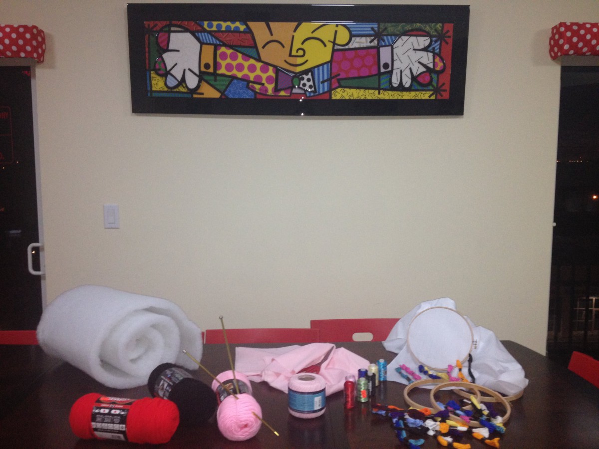 A table filled with craft supplies, including yarn, tape, and fabric, beneath a colorful artistic painting.