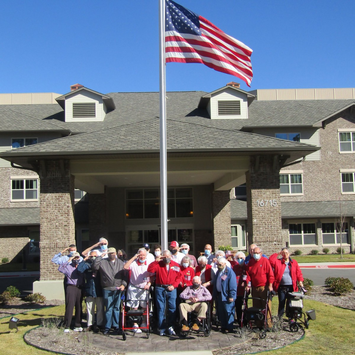 A group of seniors gathered outside a building under an American flag on a sunny day.