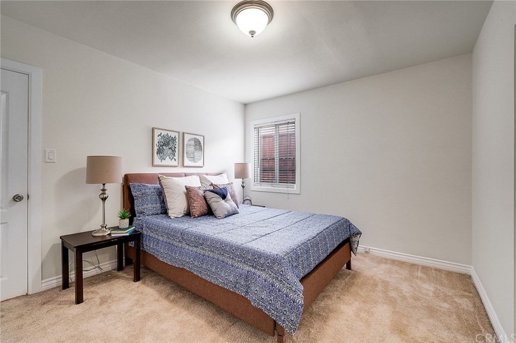 A cozy bedroom with a neatly made bed, two bedside lamps, and a window letting in natural light.