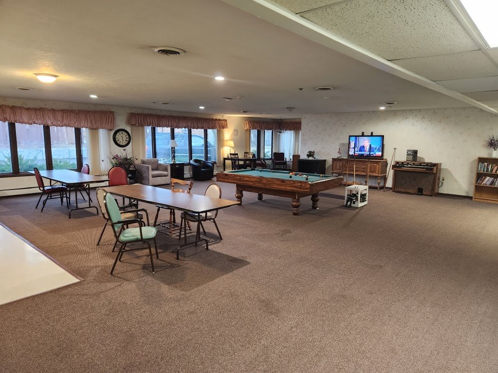 A spacious game room featuring a pool table, several tables and chairs, a television, and large windows.