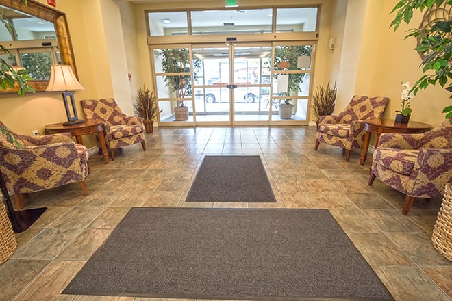 A well-lit lobby area with chairs and plants beside a carpeted entrance.