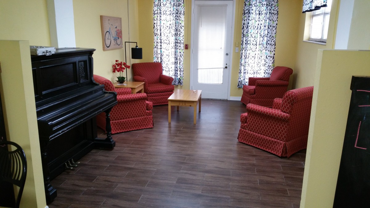 A cozy living room featuring a piano, red upholstered chairs, and wooden flooring.
