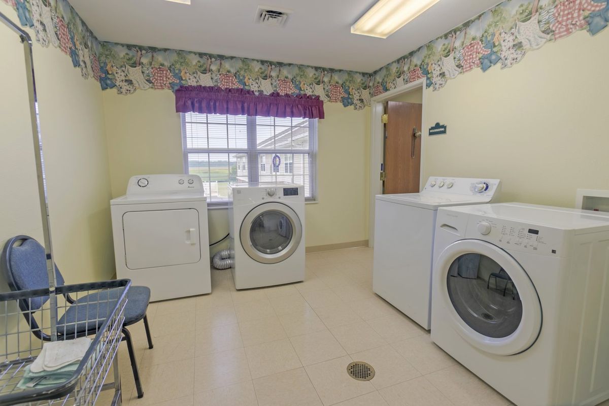 A laundry room with multiple washing machines and a dryer, featuring floral wallpaper and a window for natural light.