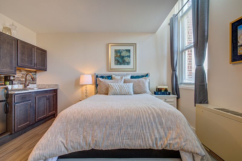 A cozy bedroom with a neatly made bed, flanked by a lamp and window, featuring decorative artwork above the headboard.